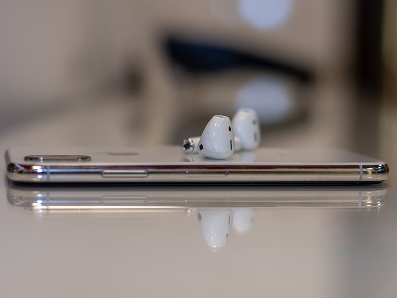 silver smart phone flat on table with white AirPods resting on top