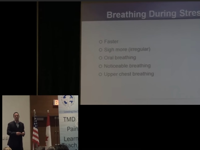 Patrick McKeown on a stage with a slide in the background with the text about breathing during stress from the article