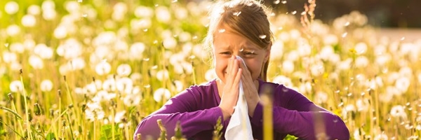 Girl sitting in a meadow with dandelions and has hay fever or allergy