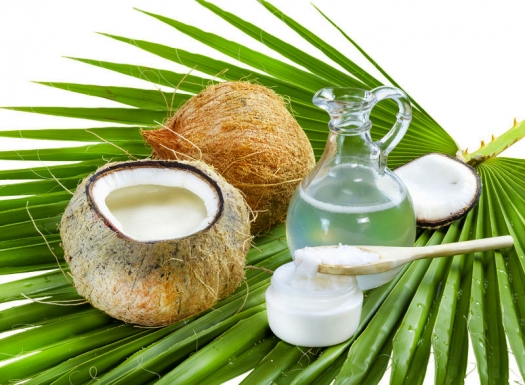 coconut, bottle and jar of coconut oil, wooden spoon on palm leaf