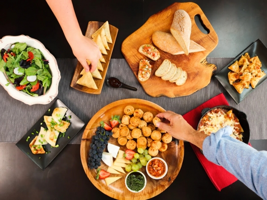 people reaching for salad, bread, fruit, finger food on table