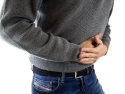 Person in blue jeans and gray sweater holding stomach in pain