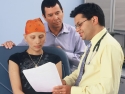 A doctor discusses medical information with a teenage girl, who is wearing a head scarf, and her father. 