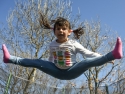 girl with pigtails doing a split in mid-air above a trampoline