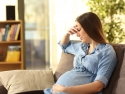 Sad pregnant woman sitting on a couch in the living room at home