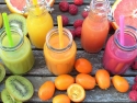 green, orange, and pink smoothies in jars surrounded by fresh fruit