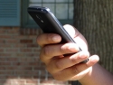 closeup of hand holding mobile phone with tree and house in background