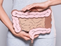 Partial view of woman holding a paper illustration of the large intestine in front of her grey T-shirt and pants