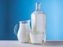 clear glass, pitcher, and bottle filled with milk on gray table and blue background