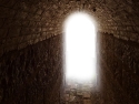 dark stone passage leads to arched opening with white light  