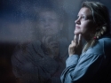 sad woman looking out a dark window covered with rain drops
