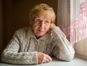 An elderly woman sits alone near a window