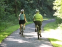 two women bicycling along paved, wood-lined path